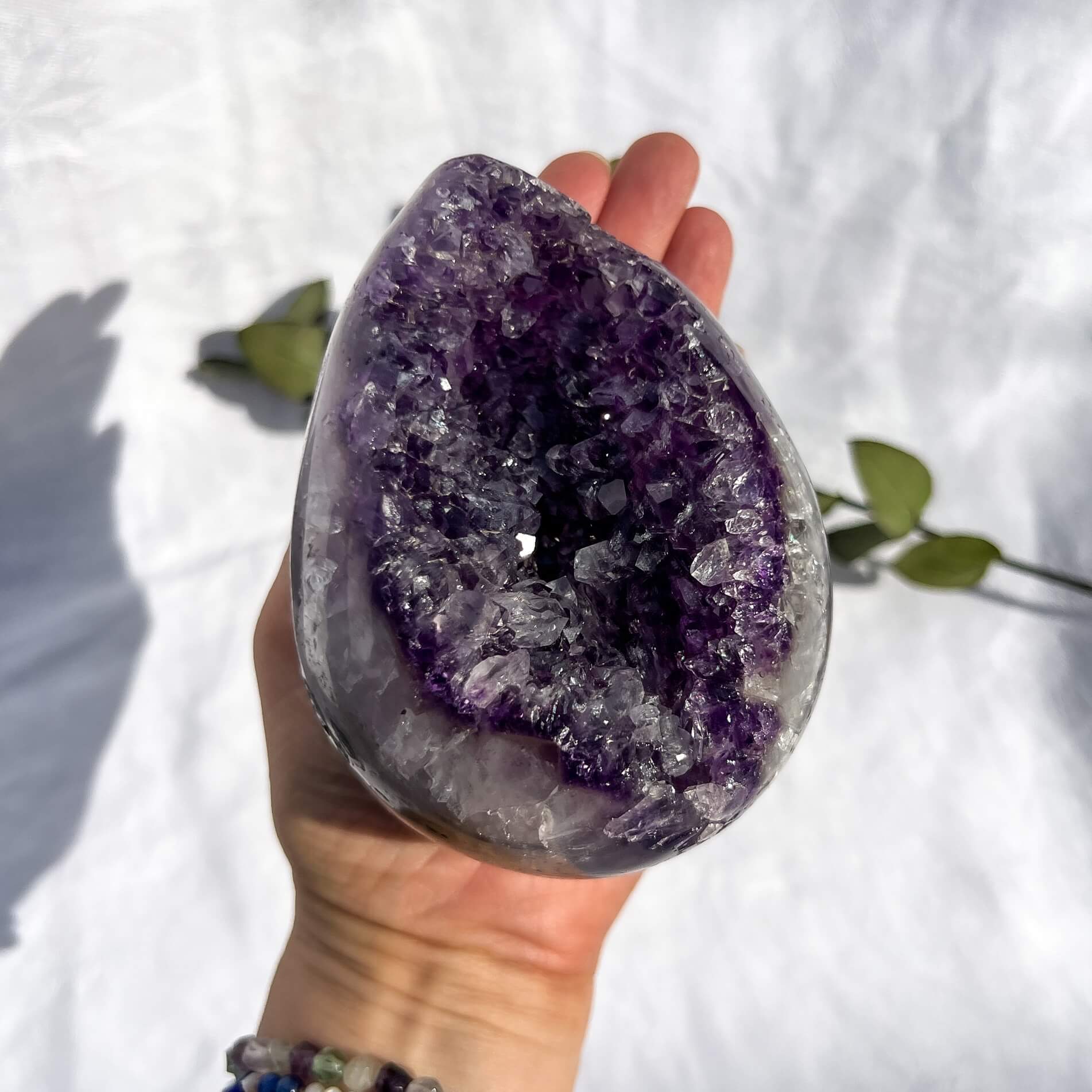 A hand holding a very large polished amethyst crystal geode egg against a white background