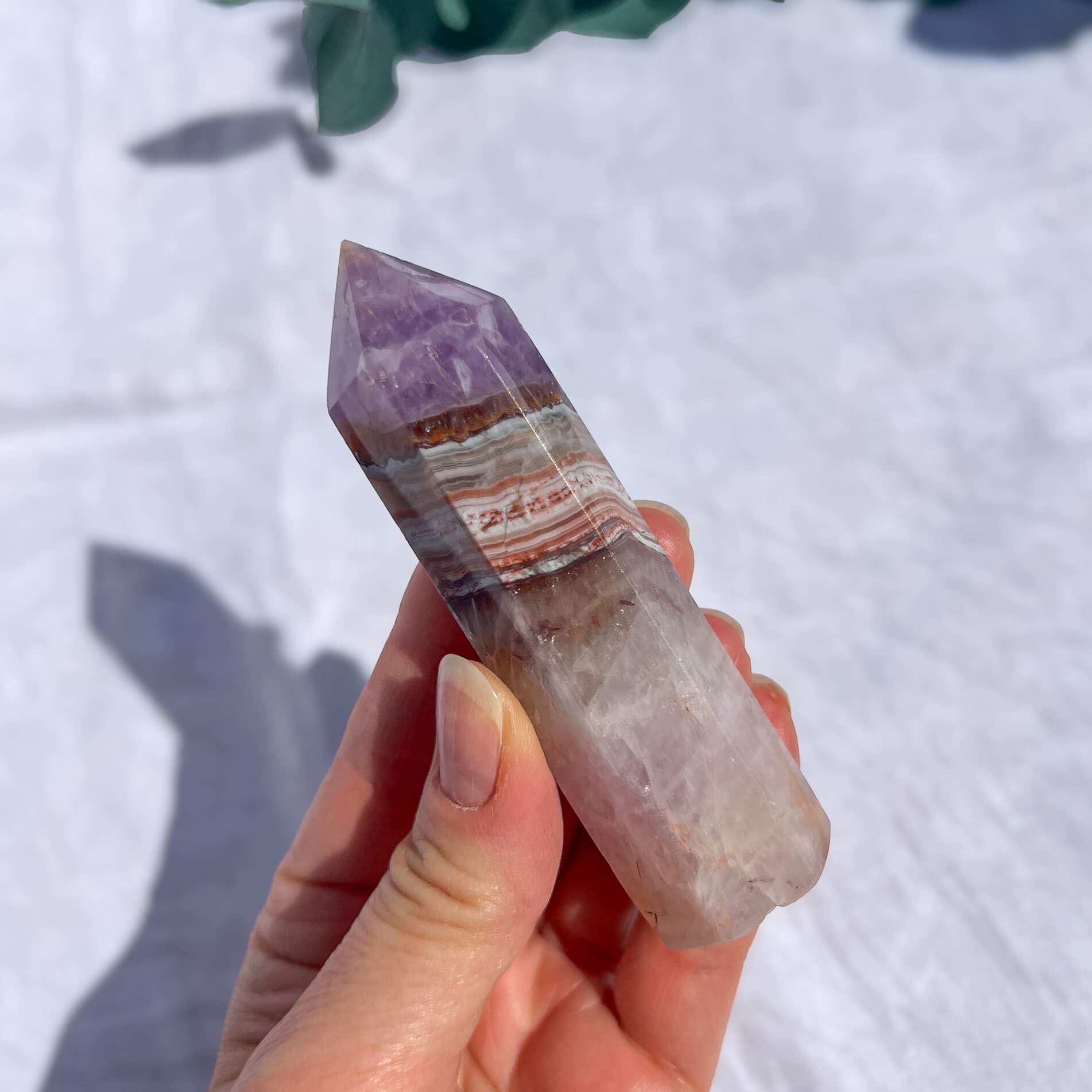 Hand holding a multicolored purple and pink striped amethyst and crazy lace agate tower against a light background