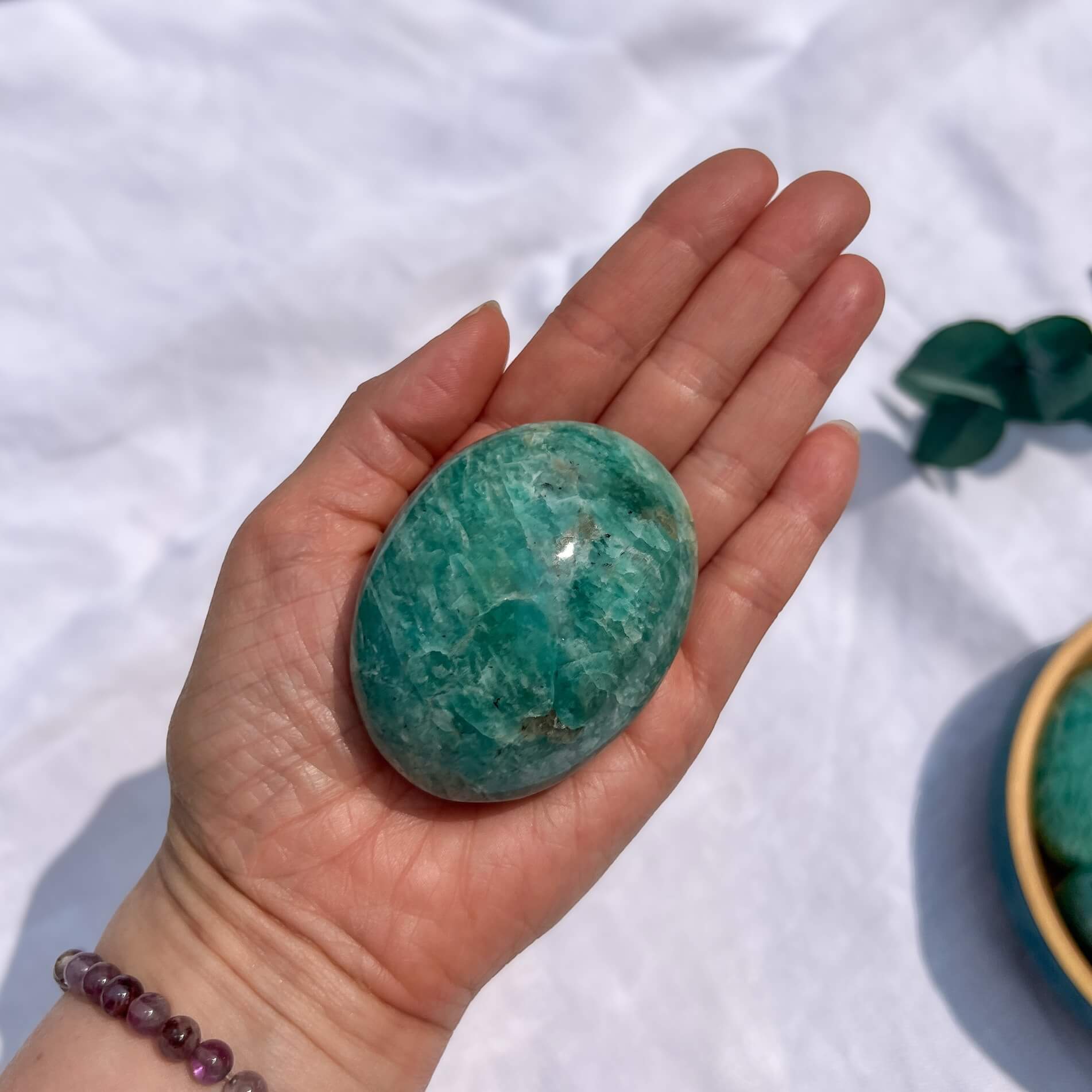 Hand holding a large turquoise amazonite crystal palmstone with a white background