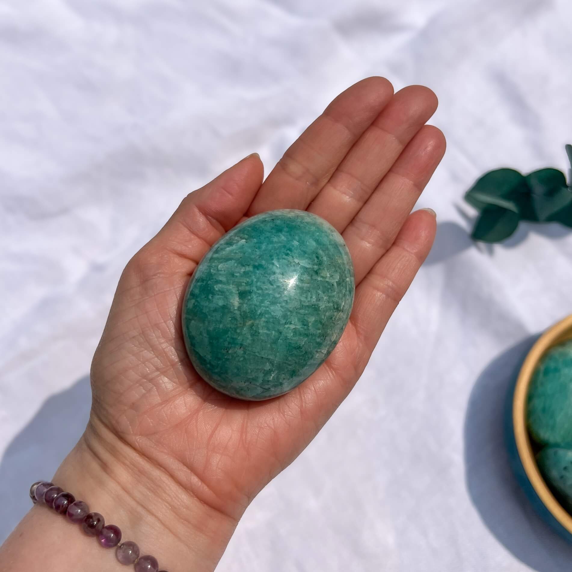 Hand holding a green amazonite crystal palmstone with a white fabric background