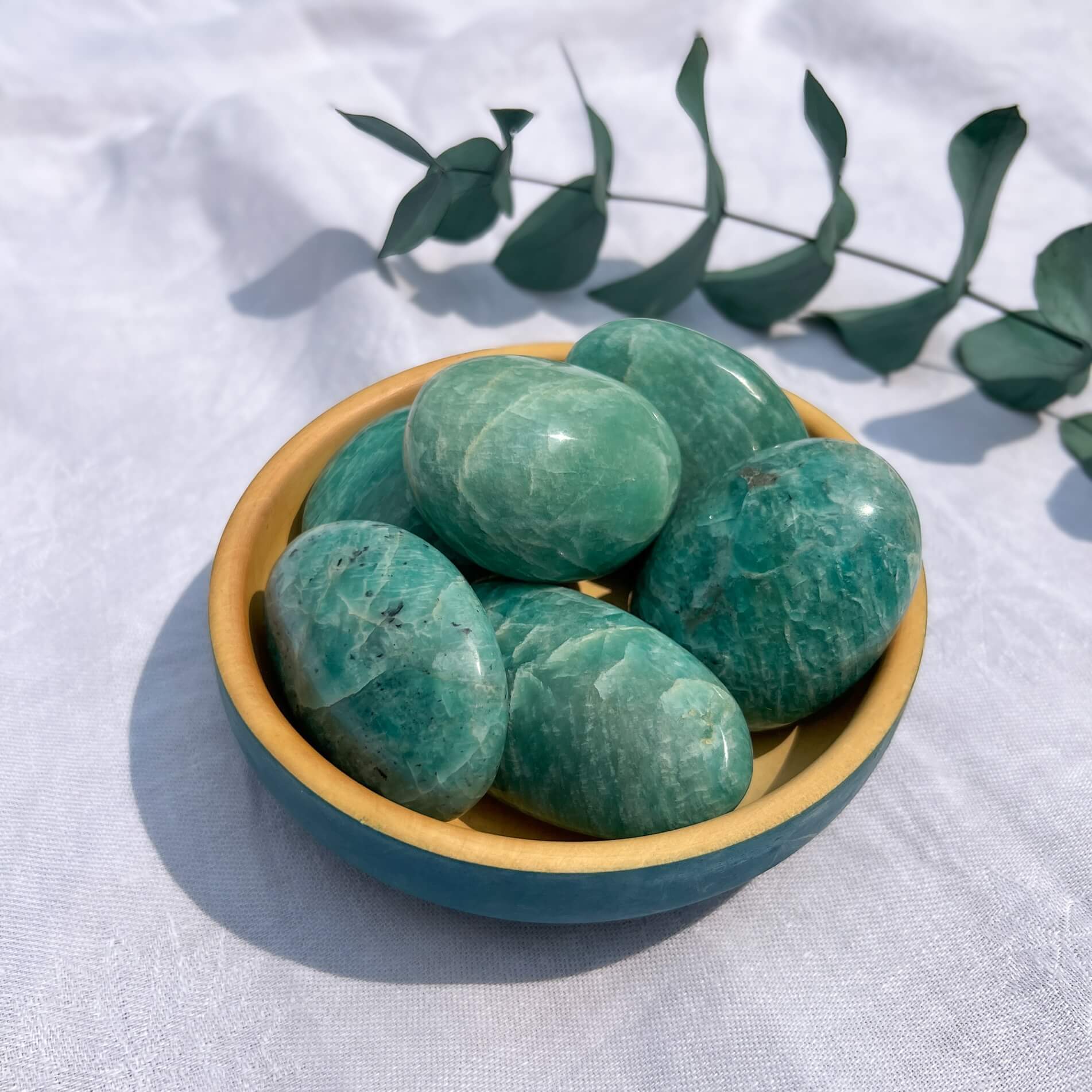 Vibrant turquoise green crystal palmstones in a blue wooden bowl on a white background with green leaves.
