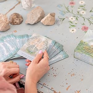 Person holding ancient stones oracle cards on a table with decorative elements