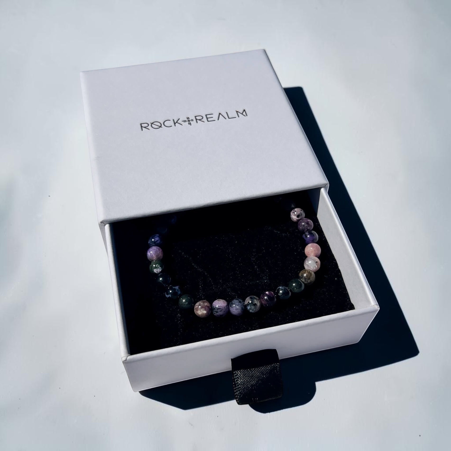 Black, Purple, grey & pink Chaorite crystal bead Bracelet in a 'Rock + Realm' box on a white background