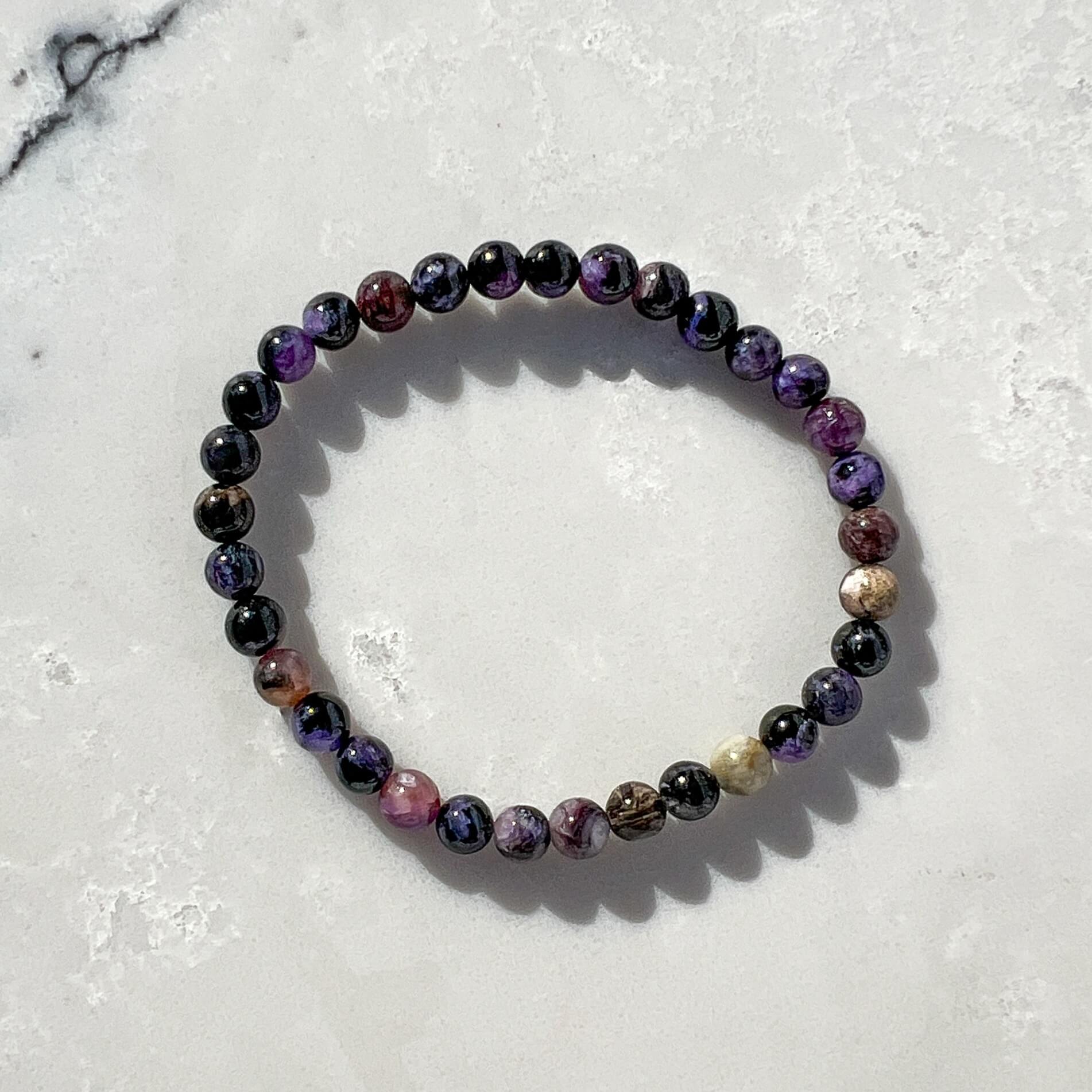 Purple, lilac and black Chaorite crystal bead bracelet on a light grey and white marble surface