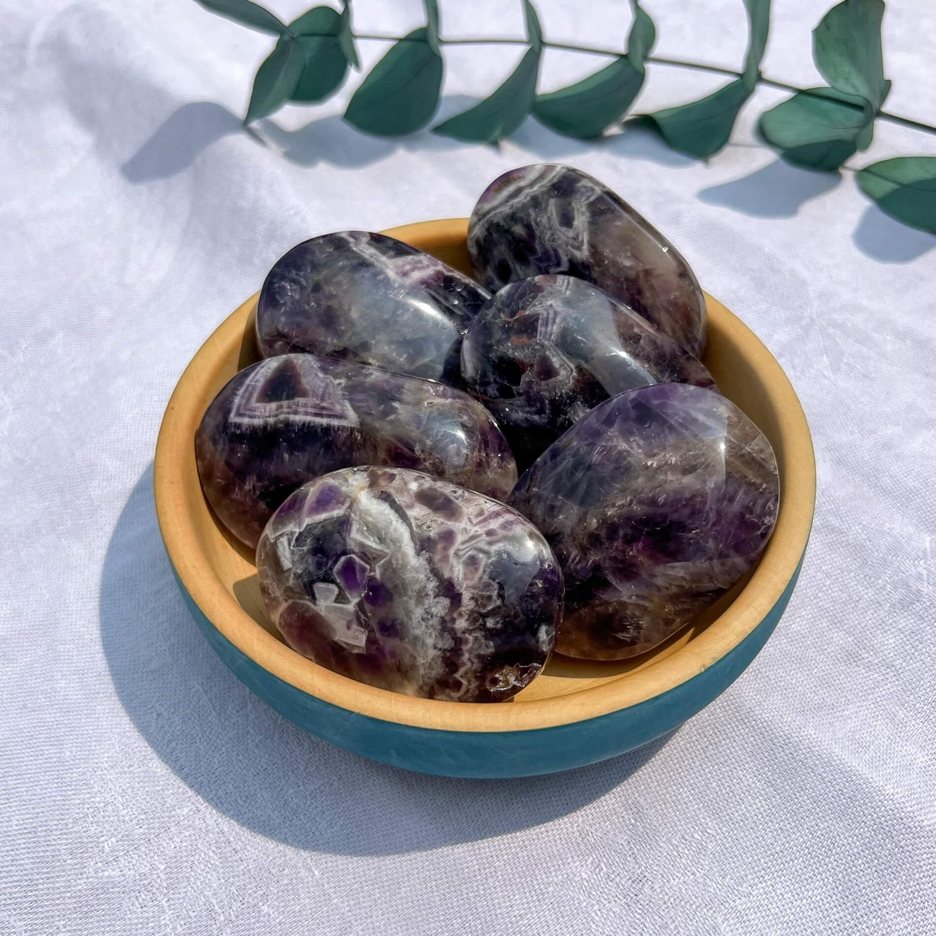 Decorative bowl with purple and white chevron amethyst crystal palmstones on a white fabric background