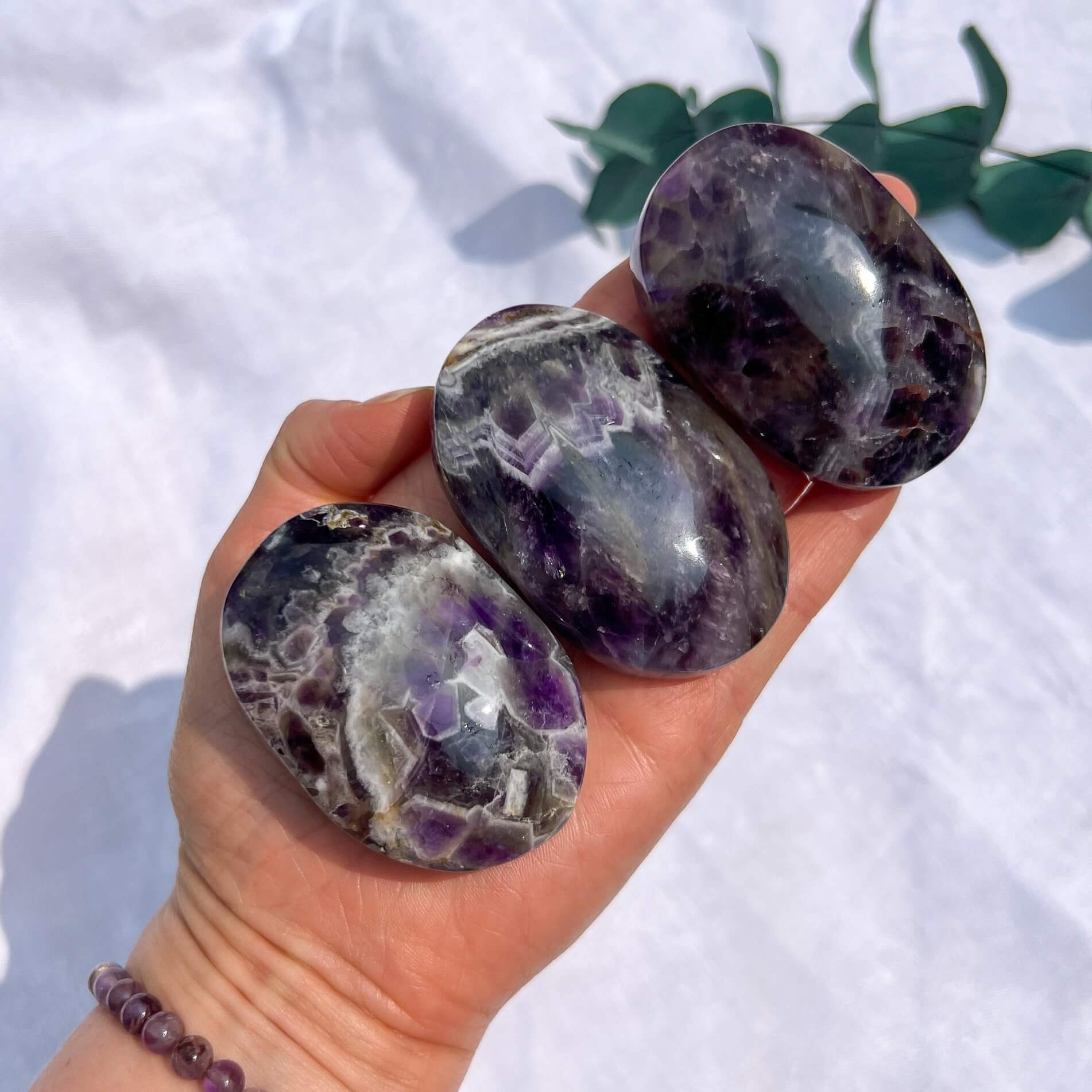 Hand holding three chunky polished amethyst palmstones against a white background