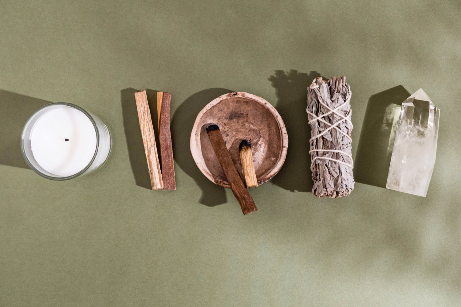 White candle, Palo Santo, sage bundle and clear quartz against a green spring background