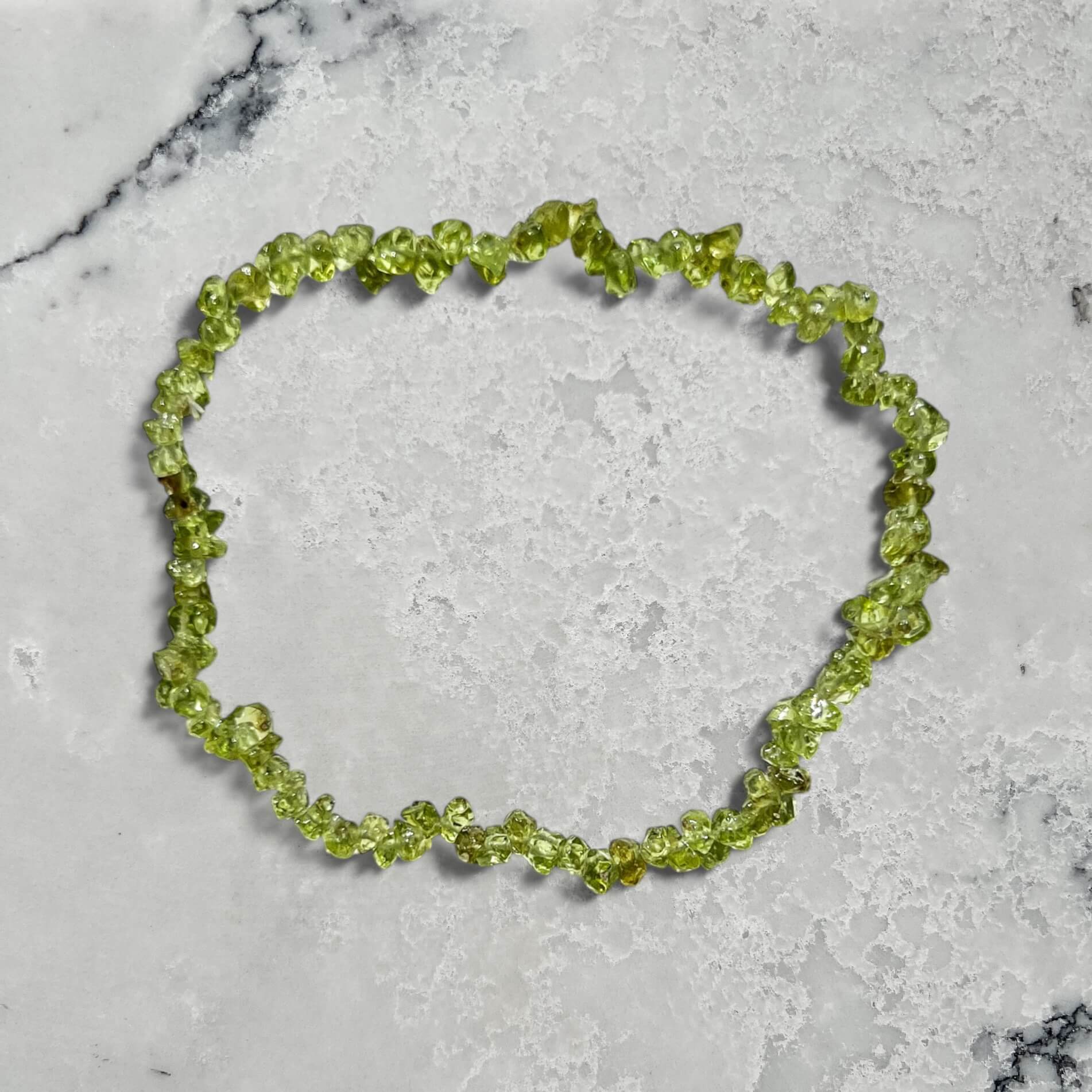 A bright green peridot crystal chip bracelet on a marble surface