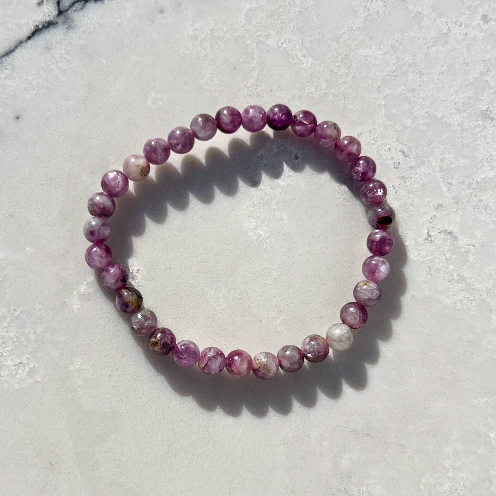 Pink and lilac Lepidolite crystal bead bracelet on a white and grey marble surface