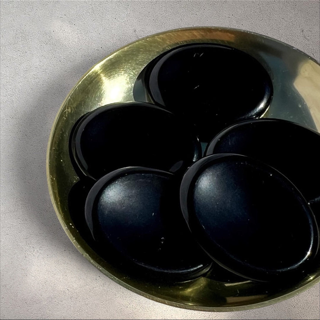 Rock + Realm Crystals polished black obsidian worry stones with thumb indentation in a brass dish.