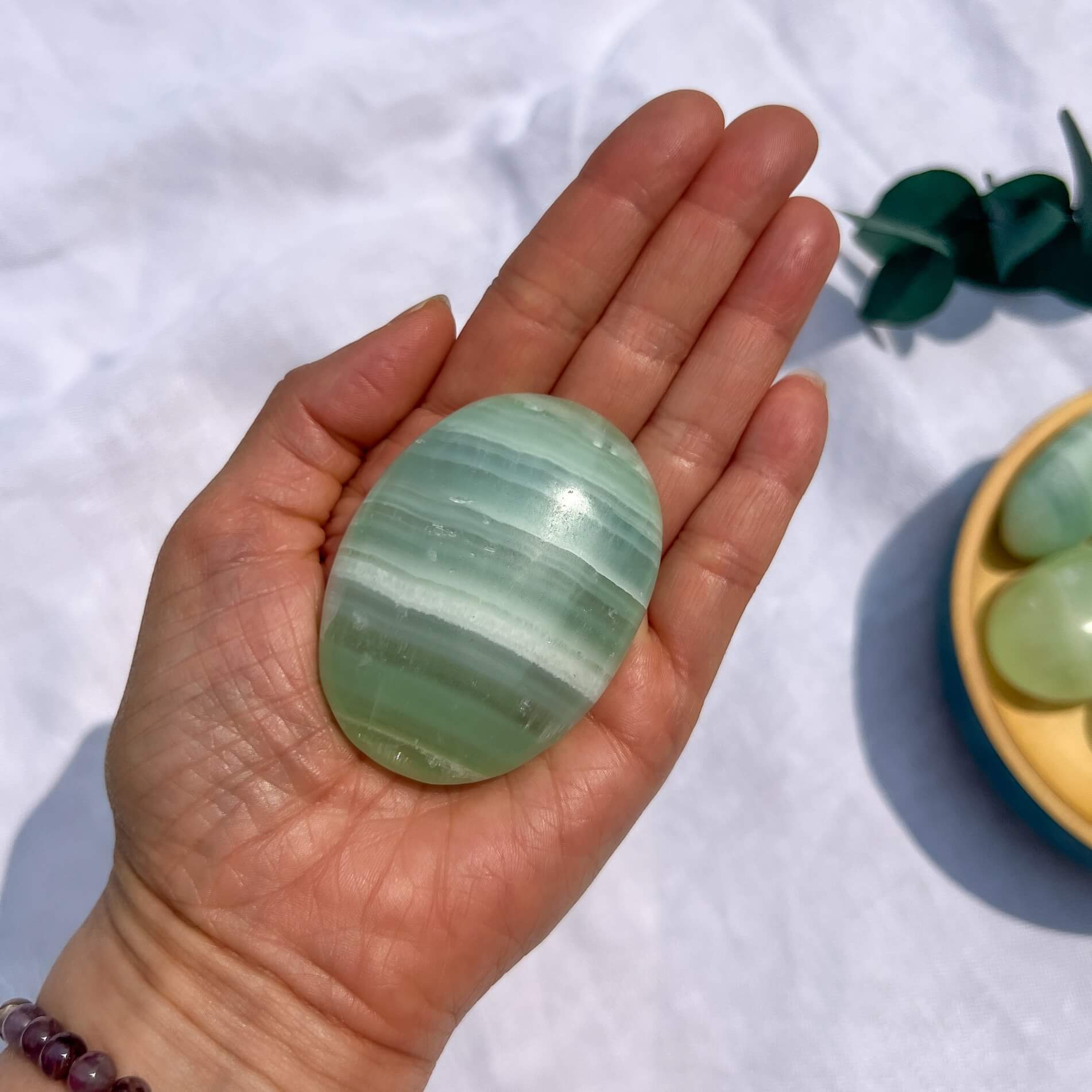 Hand holding a gummy green and white striped pistachio calcite crystal palmstone with a white background