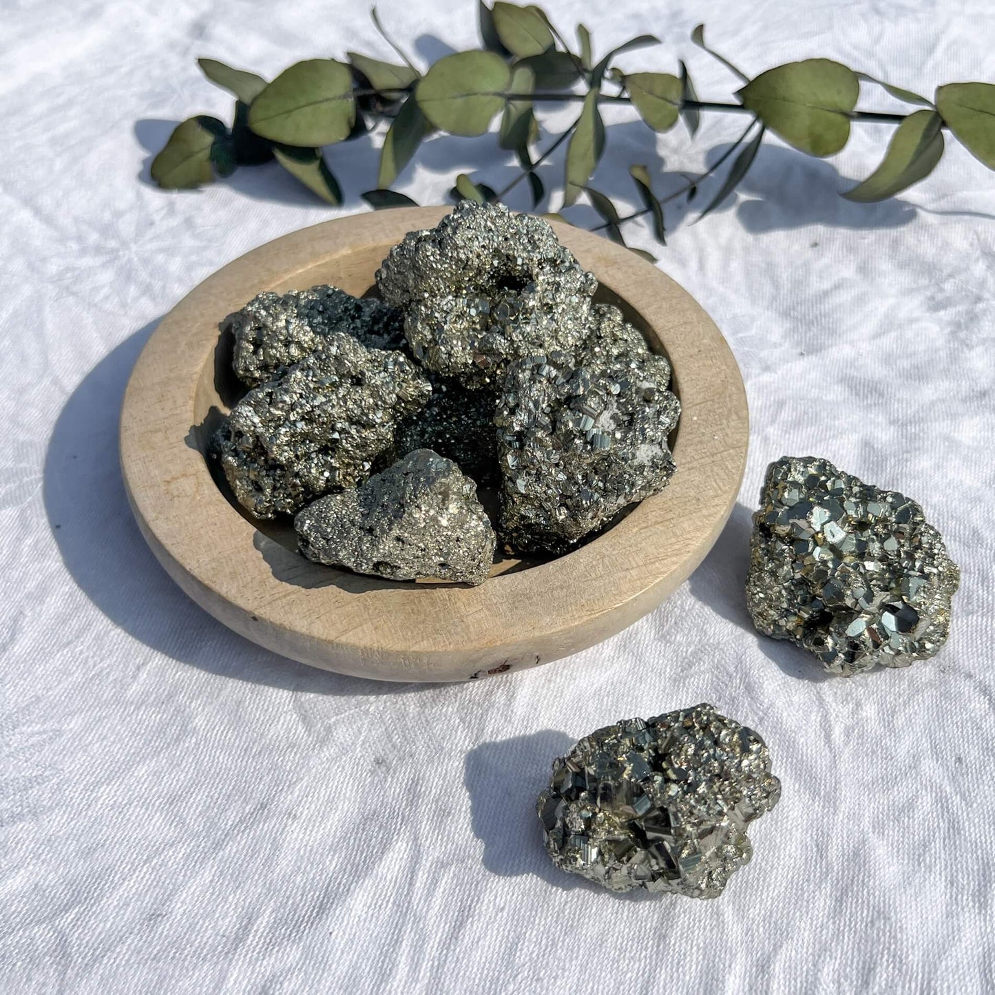 A wooden dish filled with golden sparkling pyrite crystal clusters with two displayed prominently at the front