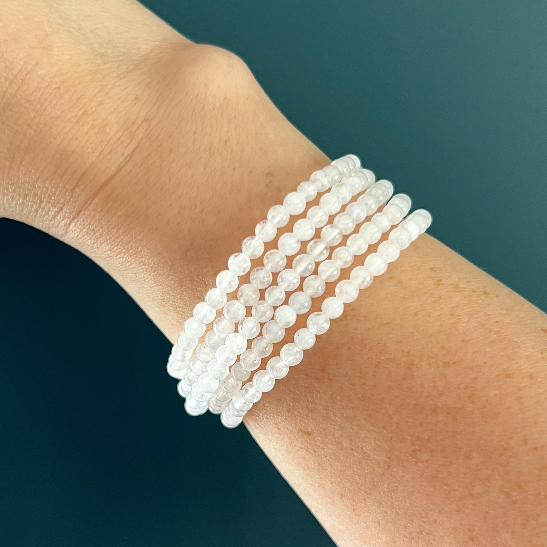 Stack of five white moonstone crystal bead bracelets on a woman's wrist against a teal background
