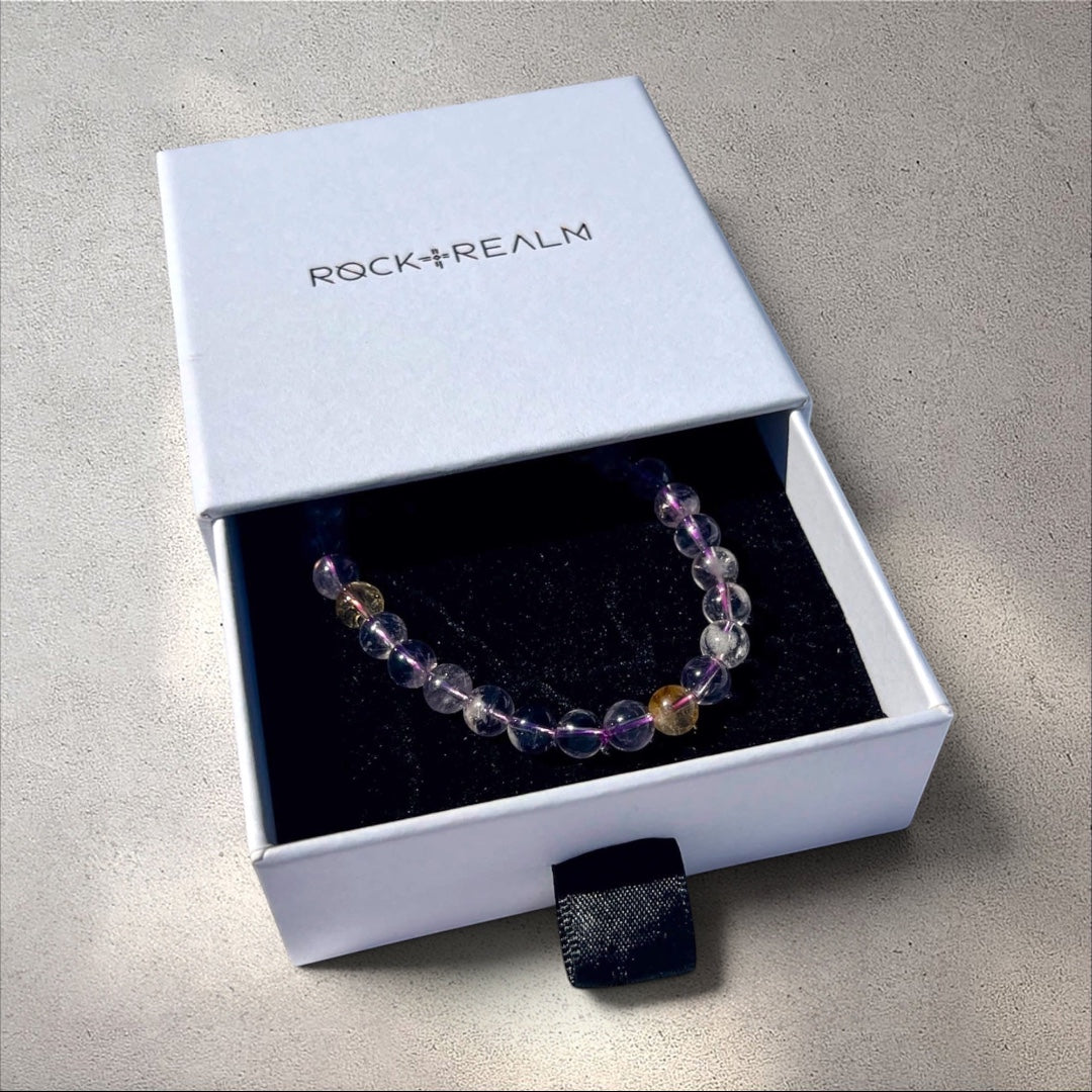 Rock + Realm Crystals Ametrine beaded bracelet with clear and purple stones in a branded white drawer pull jewellery box.