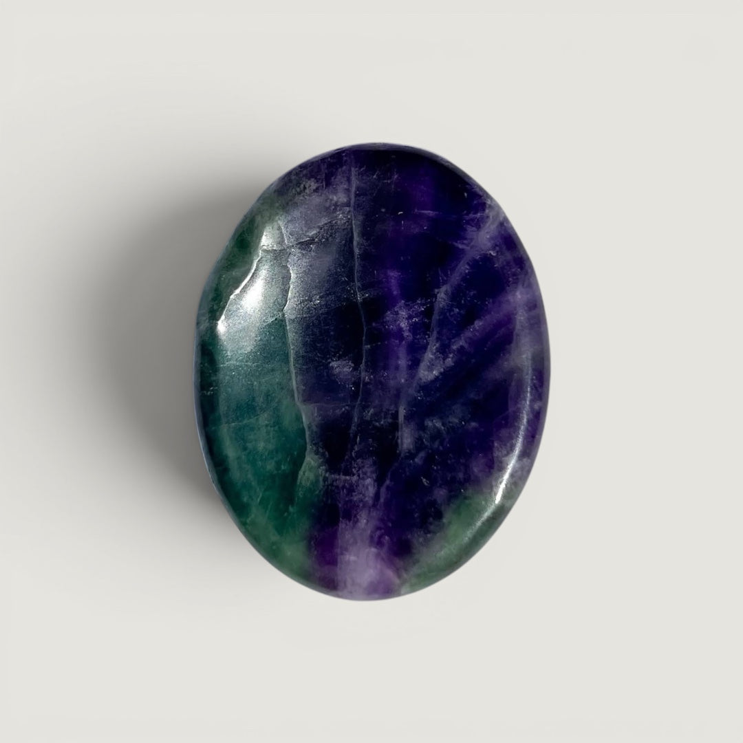 Rock + Realm Crystals polished oval fluorite worry stone with green and purple hues, featuring a thumb indentation for stress relief.