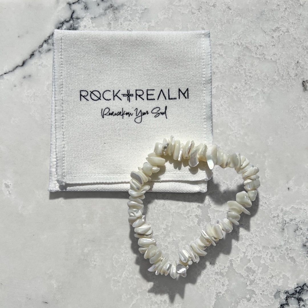 Rock + Realm white mother of pearl chip bracelet arranged in a heart shape next to a branded cloth pouch.