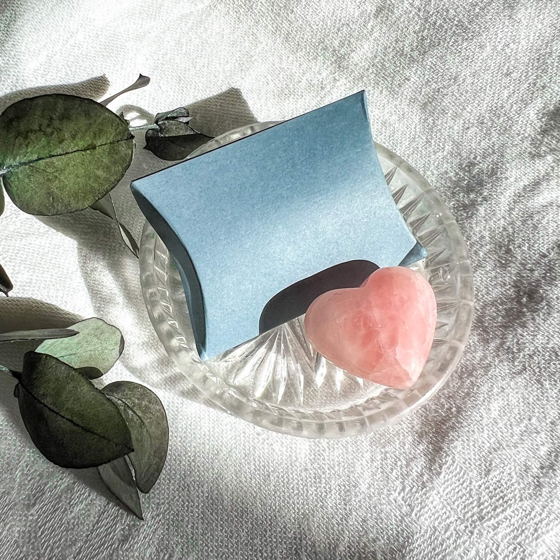 Pale pink rose quartz mini crystal heart displayed in a small glass dish with a pale blue card pillow box