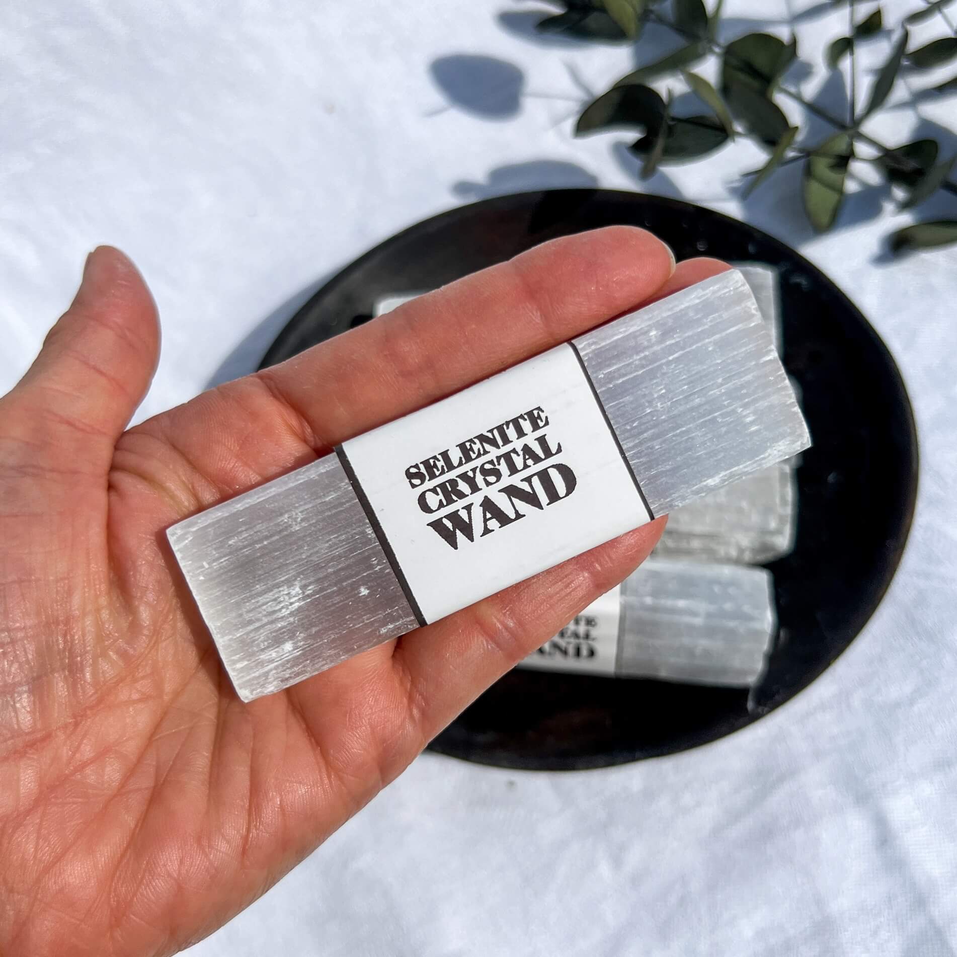 A close up of a white selenite crystal wand held in an outstretched hand