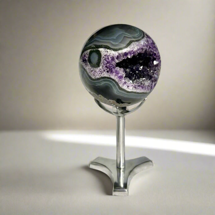 A beautiful dark purple amethyst geode sphere in a small crystal sphere holder display stand