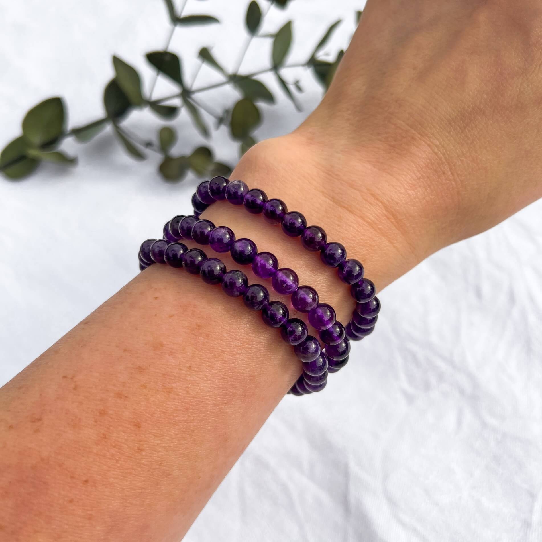 A woman's wrist wearing three bright purple amethyst crystal bead bracelets