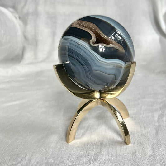 A blue swirly agate crystal sphere sits in a shiny brass claw display stand
