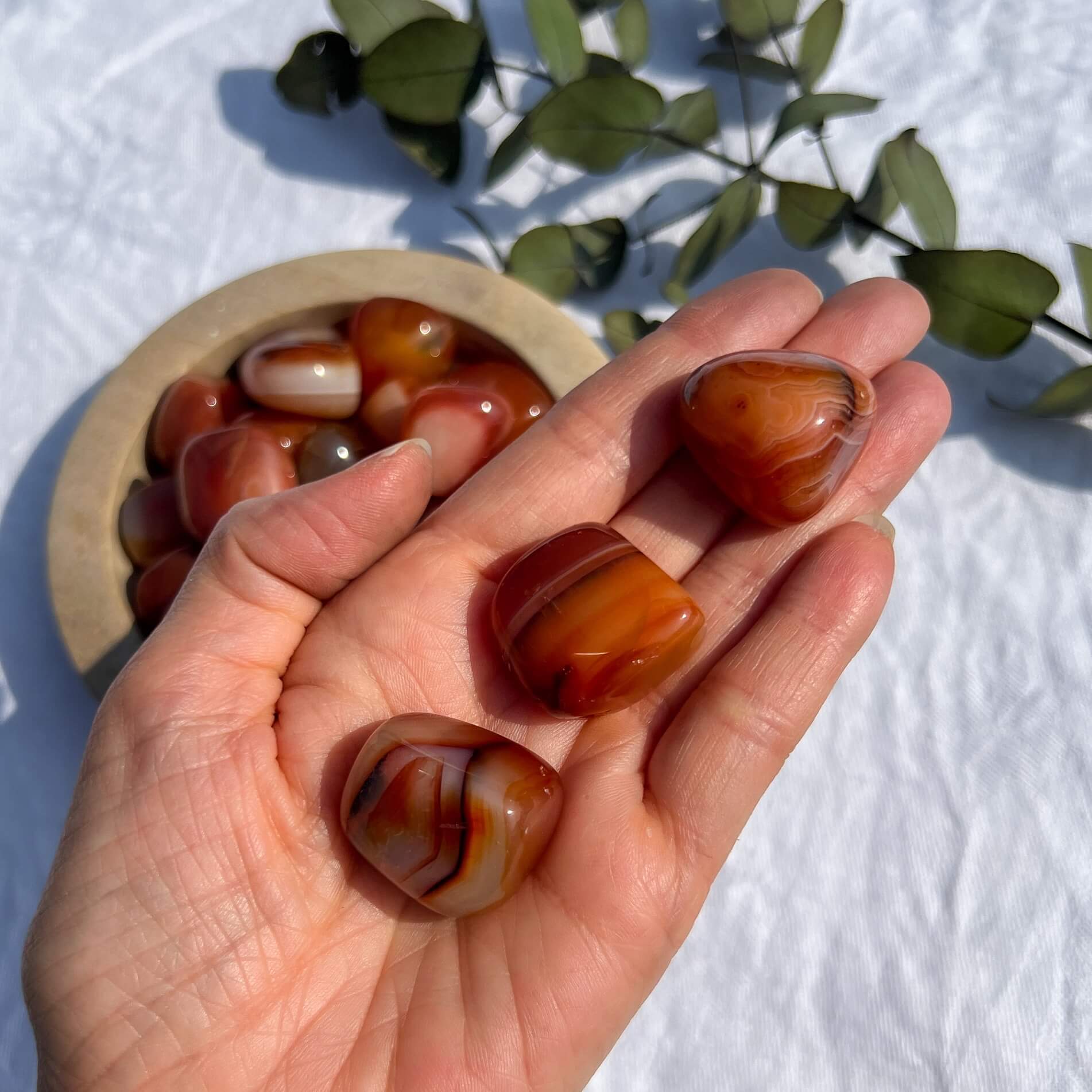 A hand filled with three deep red and orange patterned extra large carnelian crystal tumblestones