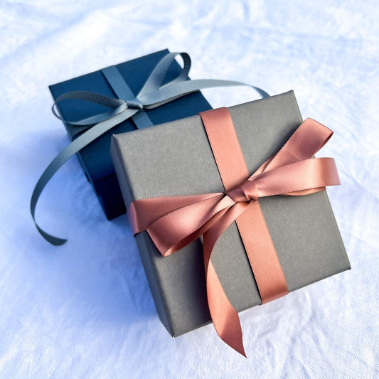 Luxury grey gift box tied in a rose gold pink ribbon with a blue gift box in the background