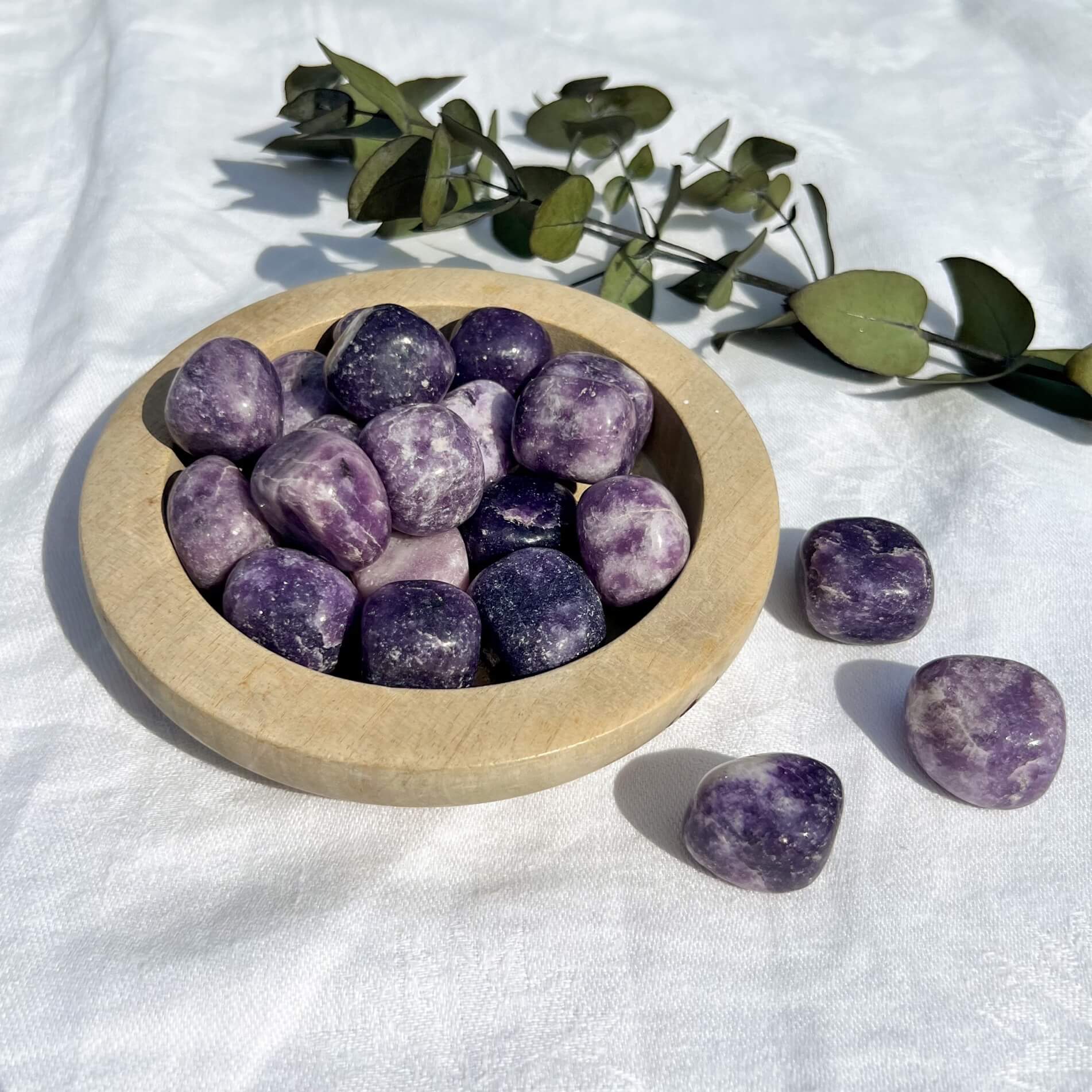 Purple and white mottle and sparkly lepidolite crystal pebbles spilling from a wooden dish
