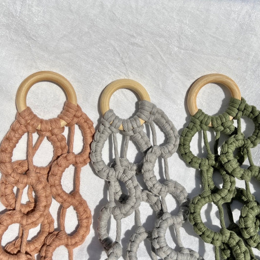 Close up of the top of 3 macrame plant hangers in pink, grey and green