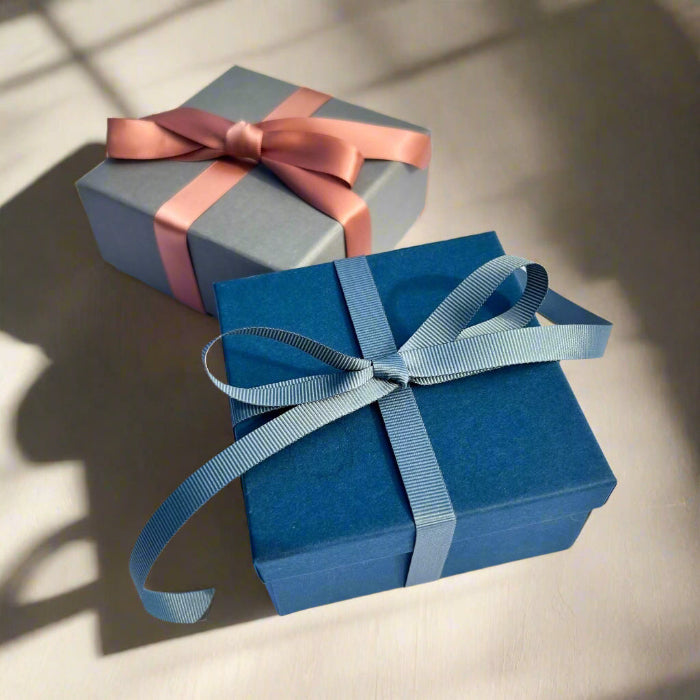 Luxury navy gift box tied in a teal grey ribbon with a grey gift box & pink ribbon in the background