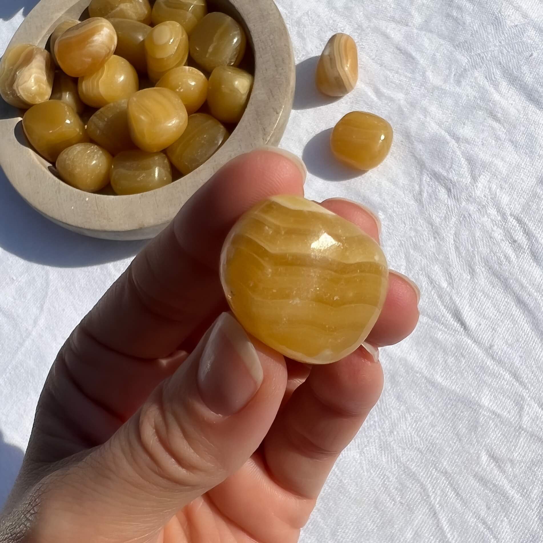 A glossy orange and honey coloured stripy Orange calcite crystal tumblestone held to camera