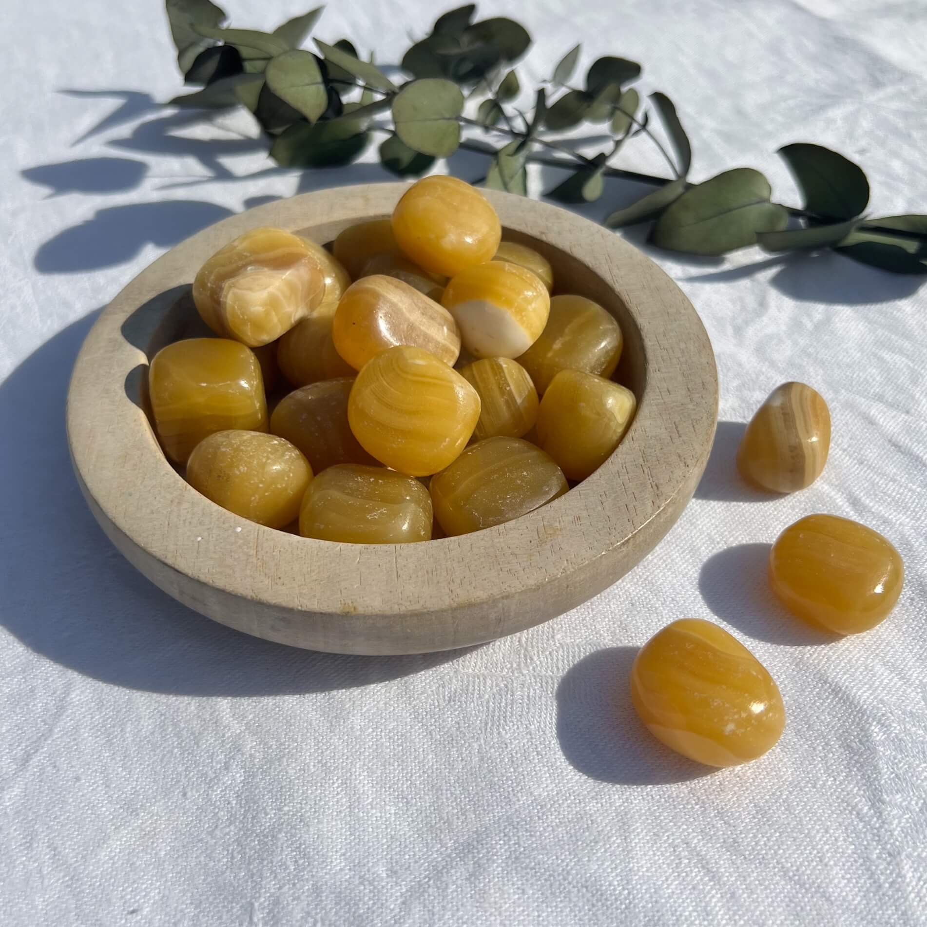 Juicy and stripey orange calcite crystal tumblestones spilling from a wooden dish and gleaming in the sun