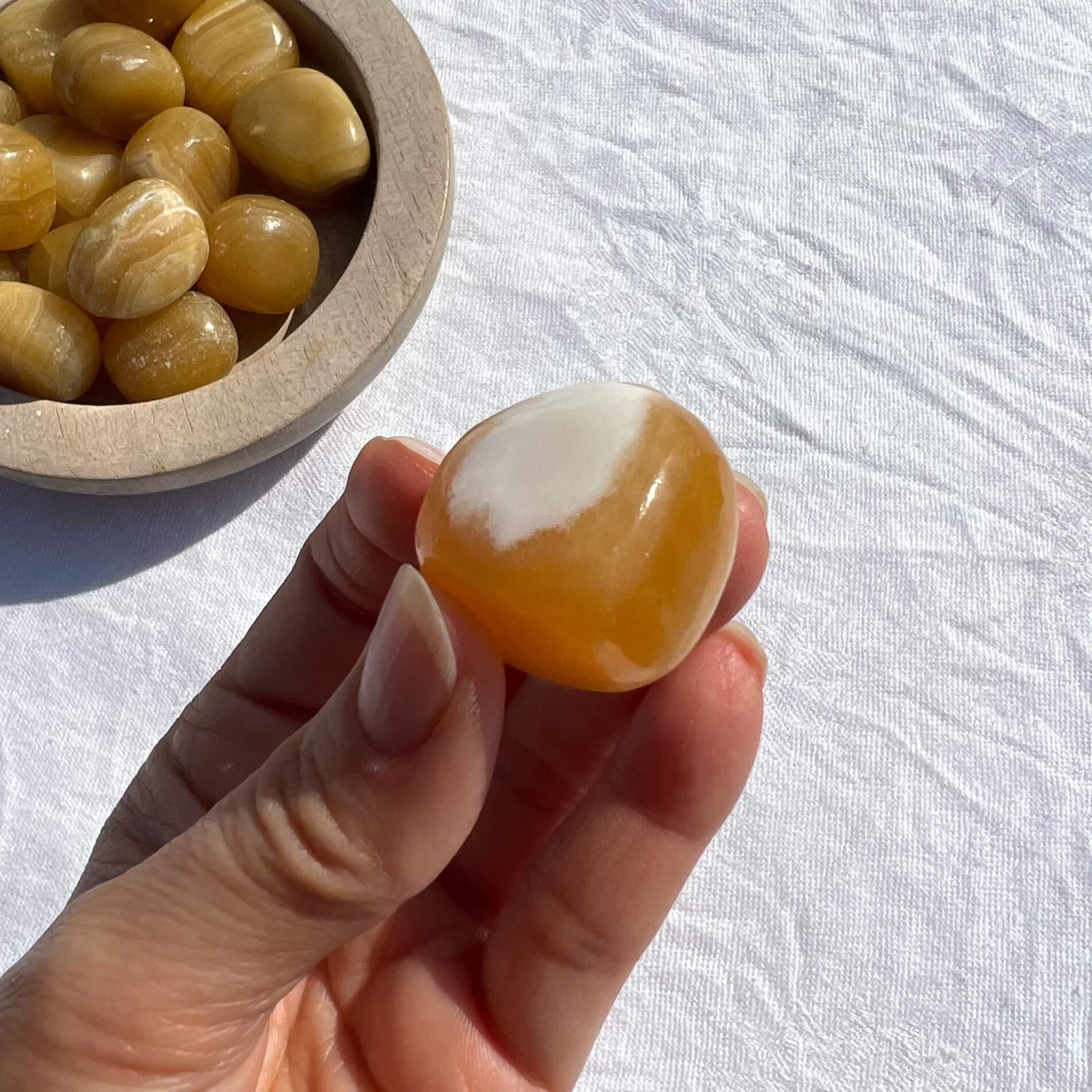 A juicy orange calcite crystal pebble held to camera