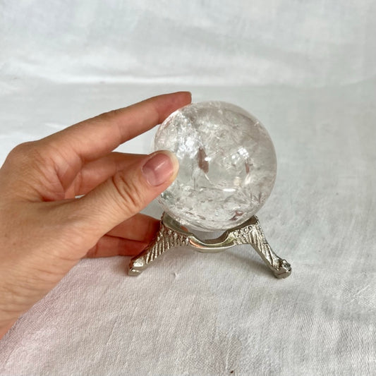 Silver nickel vintage style small crystal sphere holder with a hand touching the crystal ball sat on top