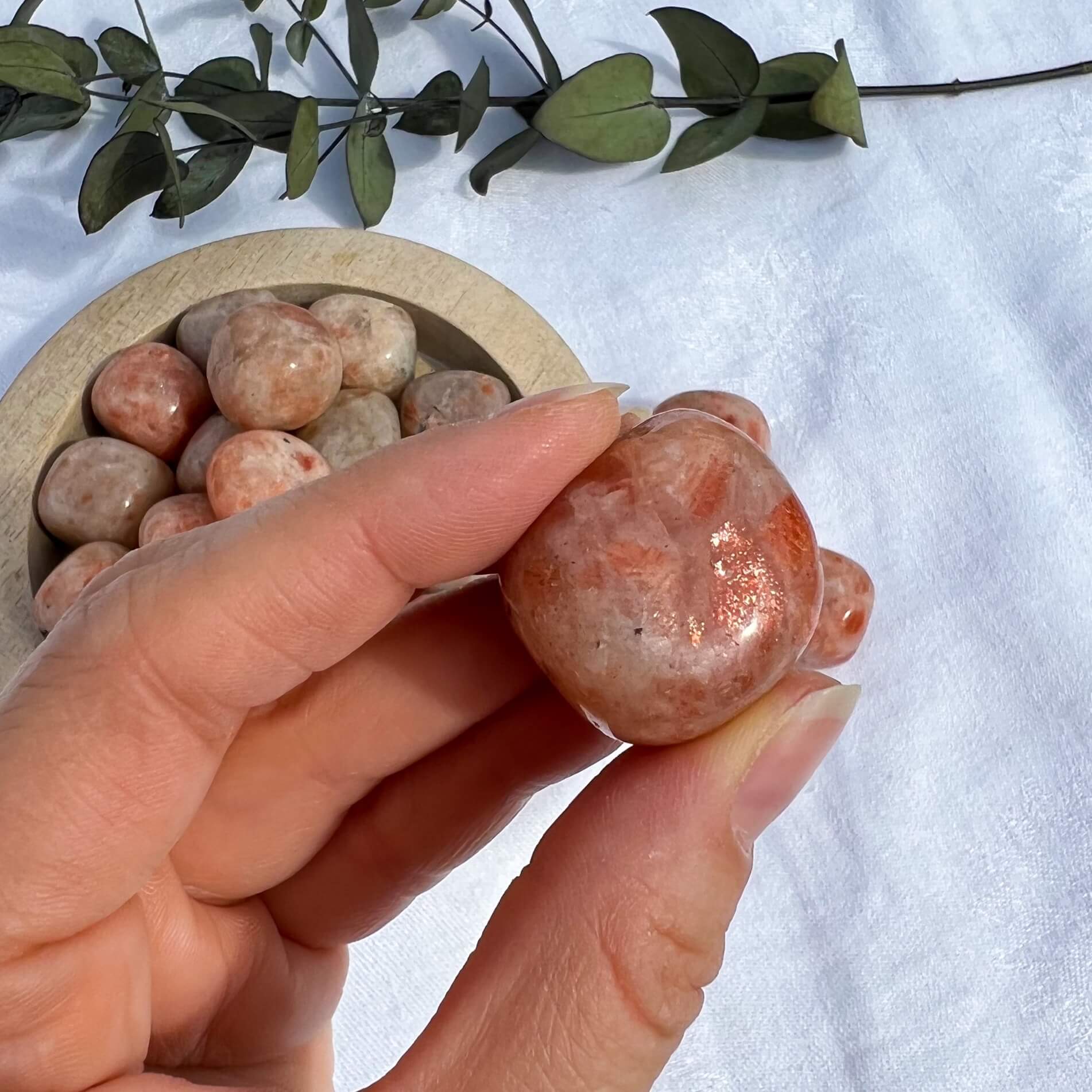 Bright orange and amber sparkly sunstone crystal pebble held to camera showing a flash