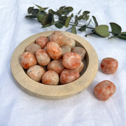 Bright orange and amber colour flashy sunstone crystal pebbles in a wooden dish