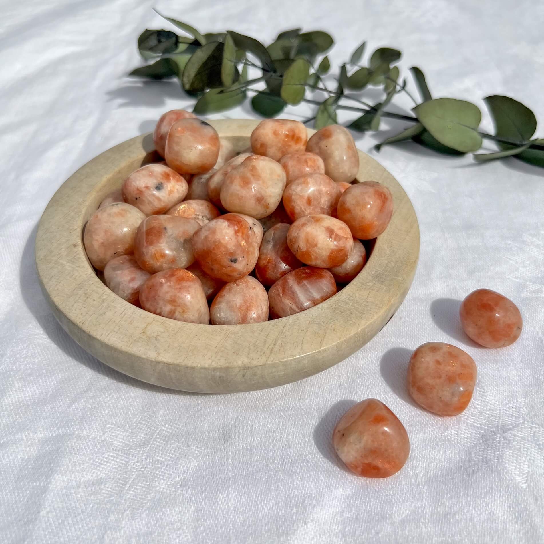 Wooden dish overflowing with bright orange sunstone crystal tumblestones