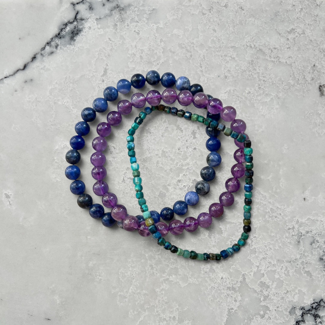 Three crystal bead bracelets in blue, purple and turquoise on a white surface