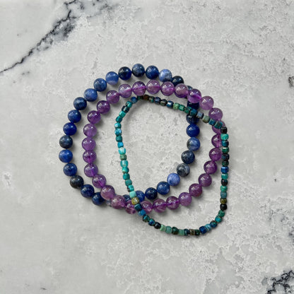 Three crystal bead bracelets in blue, purple and turquoise on a white surface