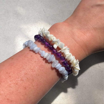 Stack of three bracelets with white mother of pearl, purple amethyst and blue lace agate beads on a wrist against a neutral background