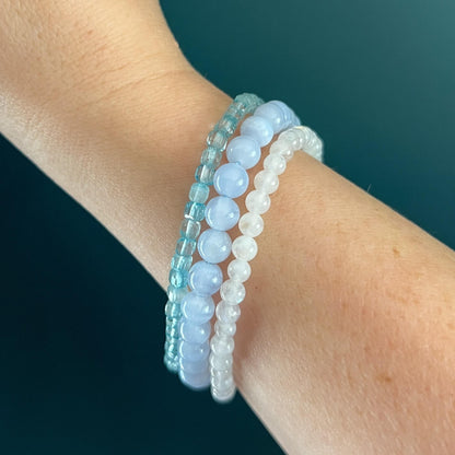 Three blue and white crystal bead bracelets on a woman's wrist against a dark teal background