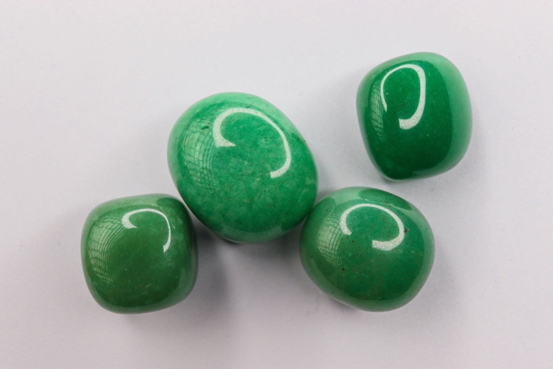 Four polished green aventurine tumblestone with a smooth, glossy finish arranged on a plain grey background.