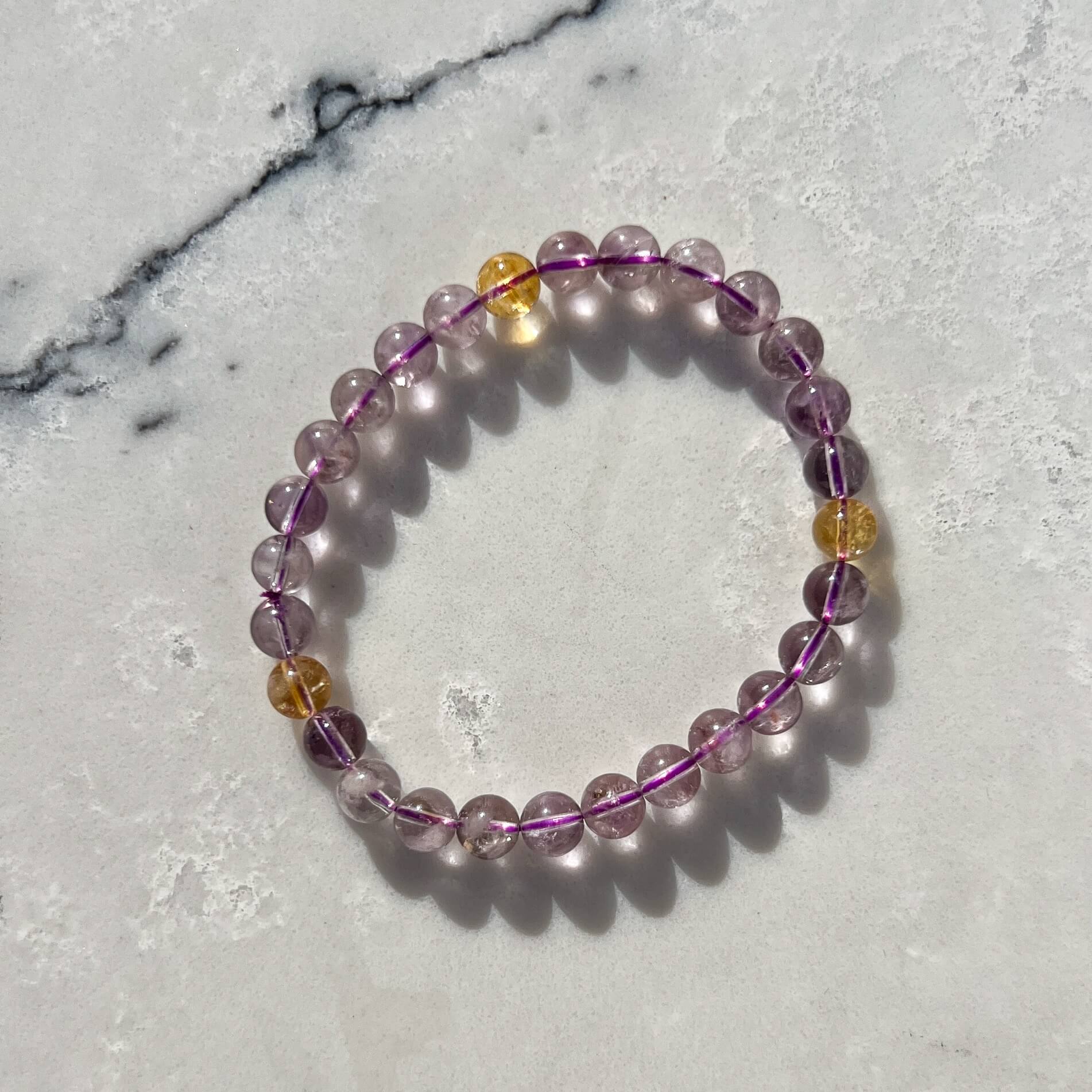 Purple and yellow Ametrine crystal bead bracelet on a white and grey textured marble surface