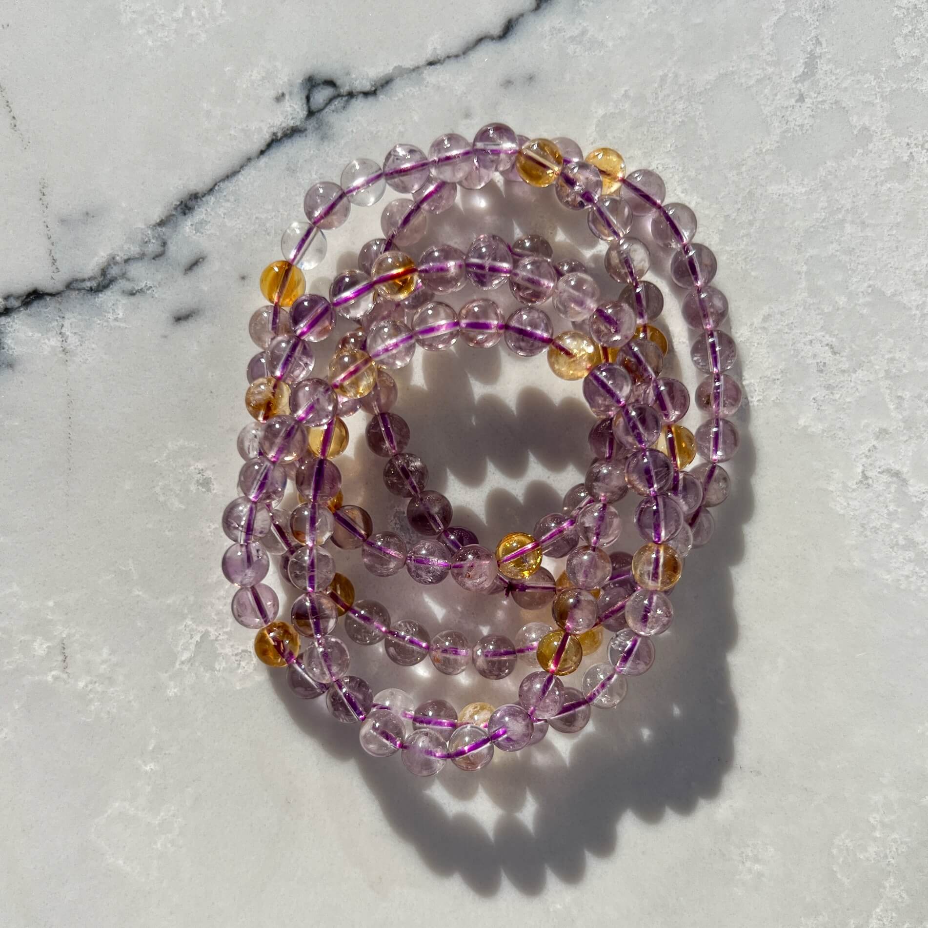 Stack of Purple and yellow Ametrine crystal bead bracelets on a marble surface