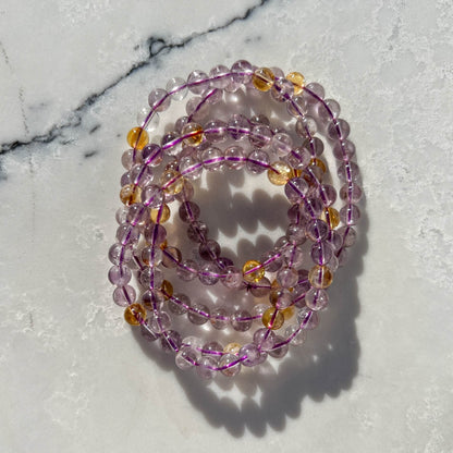 Stack of Purple and yellow Ametrine crystal bead bracelets on a marble surface