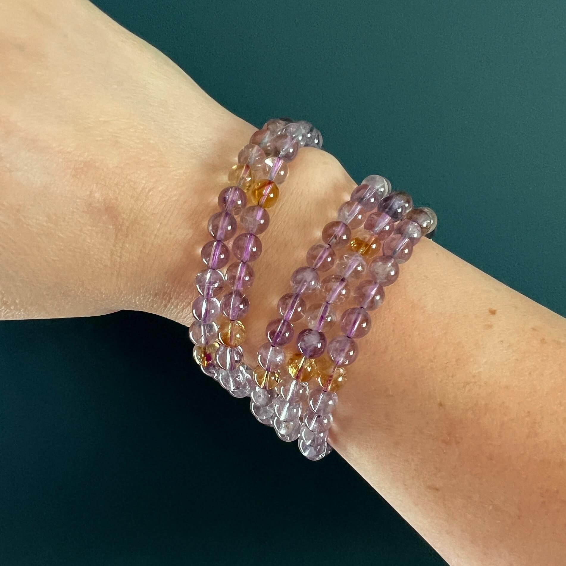 Stack of five purple and yellow Ametrine crystal bead bracelets on a woman's wrist in front of a teal backdrop