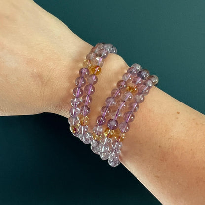 Stack of five purple and yellow Ametrine crystal bead bracelets on a woman's wrist in front of a teal backdrop