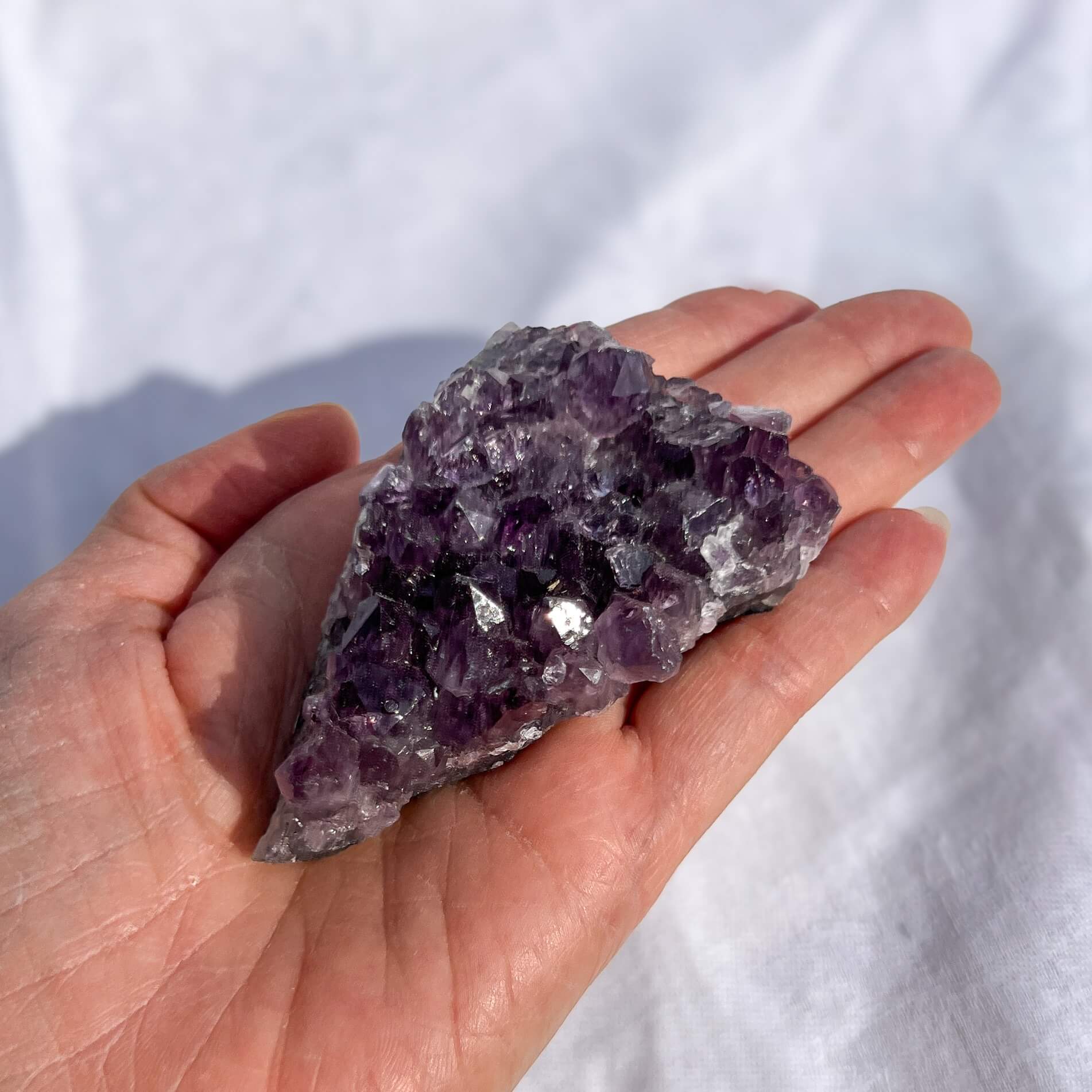 Hand holding a large amethyst crystal against a white background