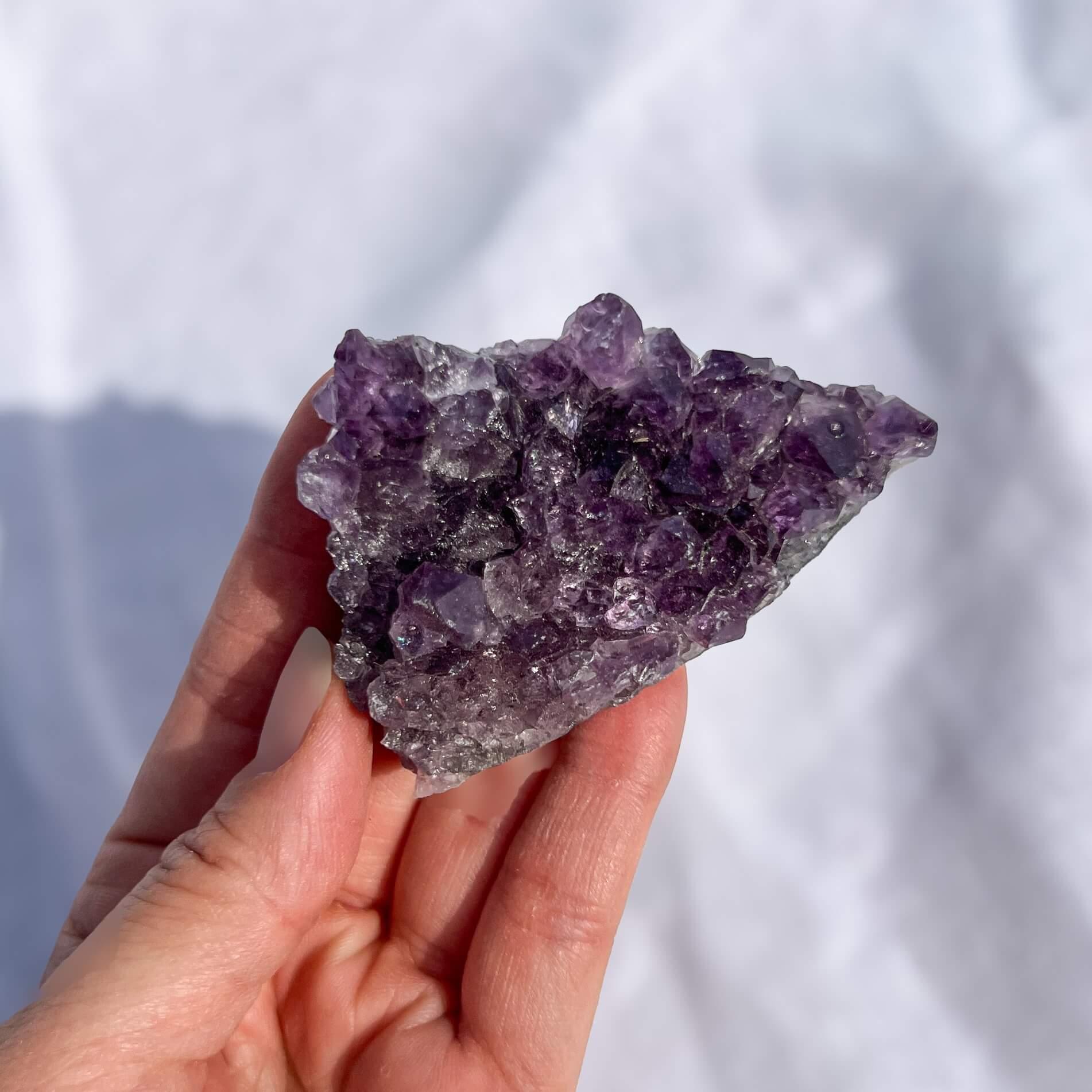 Hand holding a purple amethyst crystal against a white background