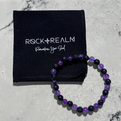 Black lave and purple amethyst crystal bead bracelet on a marble surface with a black cotton 'Rock + Realm' branded jewellery pouch